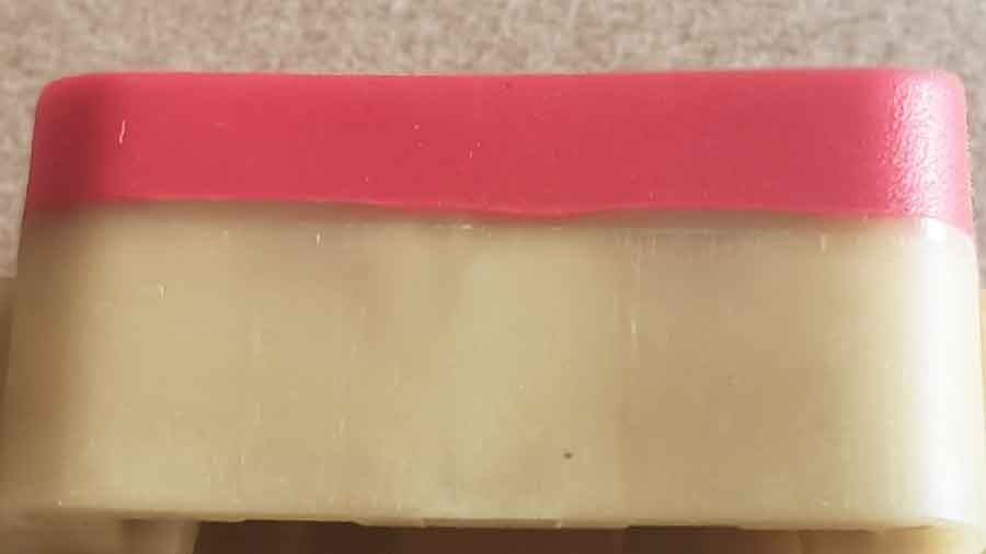 Close-up image of a red TPU layer overmolded onto a beige POK substrate, showing a visible interface transition zone that indicates enhanced polymer diffusion due to increased wall thickness.