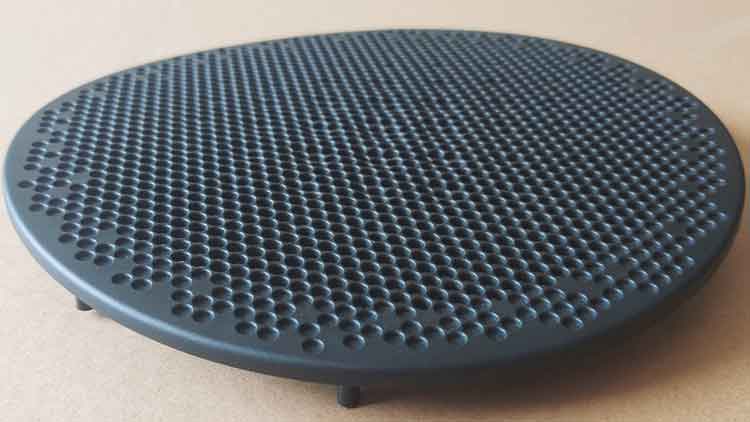 Angled front close-up of round PP plastic speaker cover showing designed curvature and smooth perforated surface