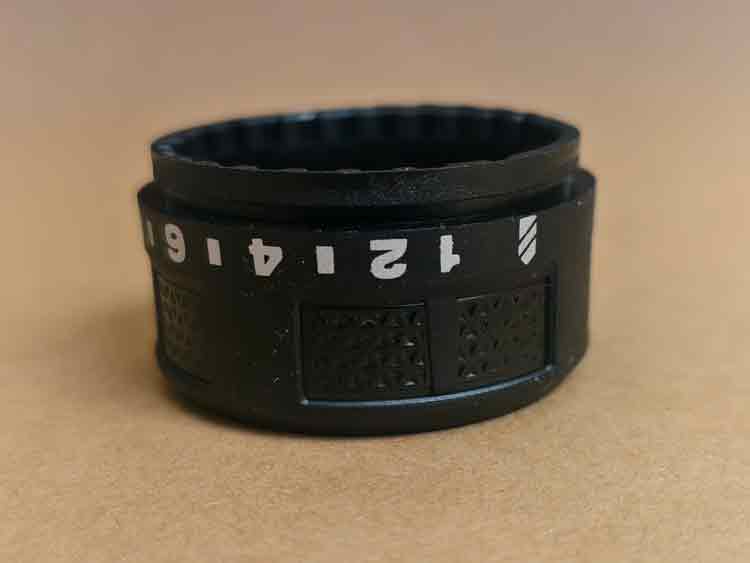 Front view of a plastic adjustment knob with scale markings printed on the surface, featuring a textured design for better grip.