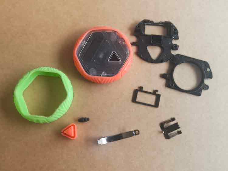 Disassembled custom plastic toy showing injection-molded plastic parts, silicone compression-molded sleeve and other components, and small stainless steel stamping components.