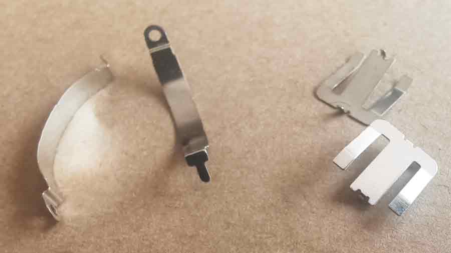 Two small stainless steel stamped parts used as battery electrodes in the custom plastic toy, showing precise shape and clean edges.