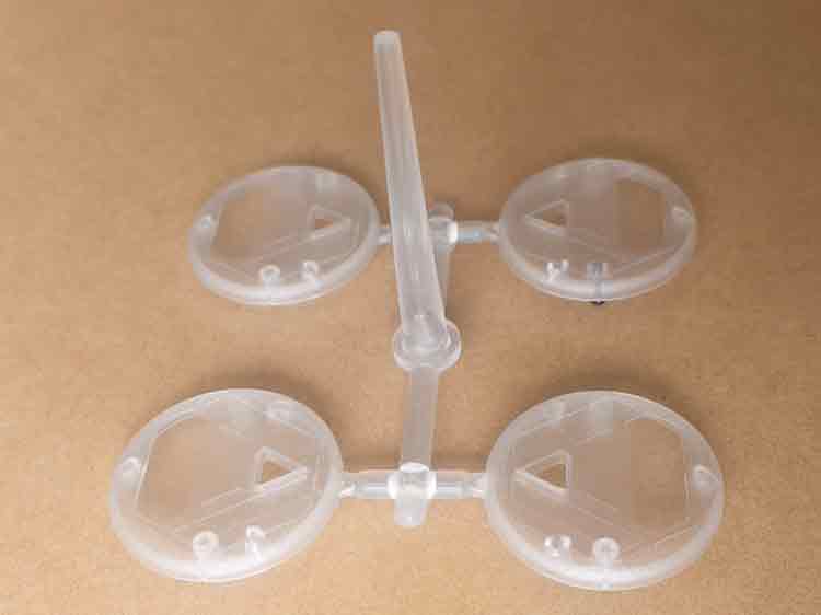 Freshly molded transparent covers for the custom plastic toy shown connected by the sprue from a four-cavity injection mold with edge gates.