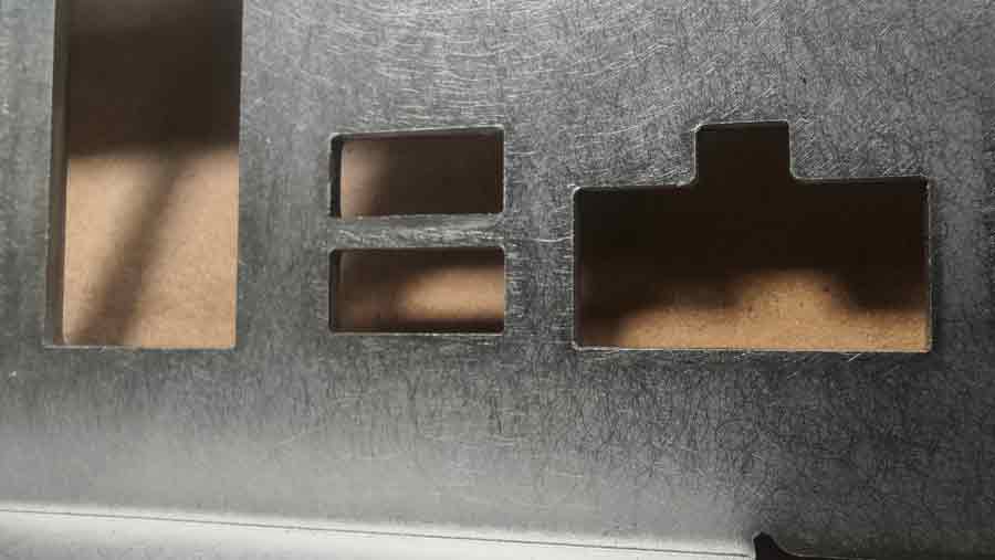 Vue rapprochée de la face arrière d'une pièce emboutie en acier inoxydable, présentant une surface polie avec un motif de grain aléatoire et des trous pour des connecteurs électroniques.