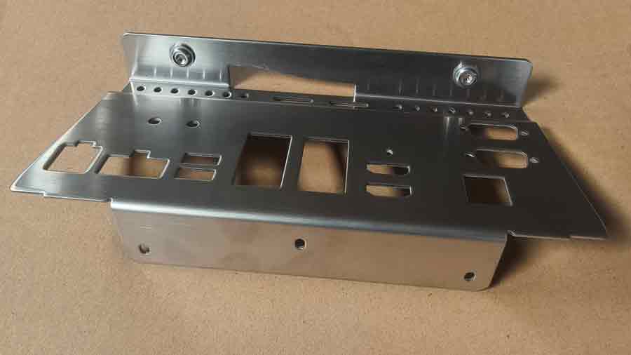 Face avant d'une pièce emboutie en acier inoxydable avec des inserts d'écrous flottants, montrant le film de protection et la finition de surface de haute qualité.