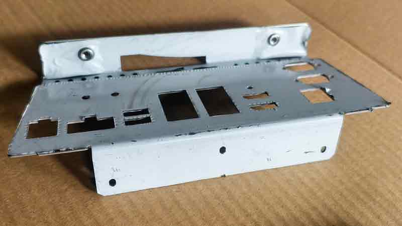 Face avant d'une pièce emboutie en acier inoxydable, avec le film de protection encore en place, montrant les coudes terminés et les écrous flottants installés.