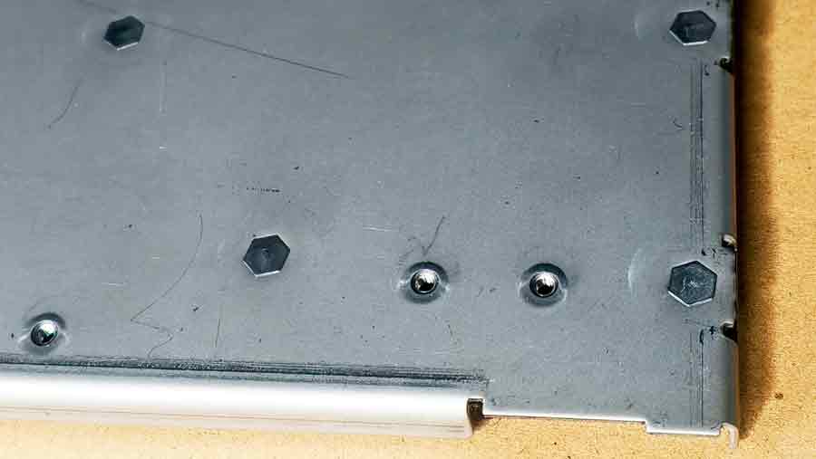 Vue arrière rapprochée d'une pièce emboutie sur mesure montrant des écrous auto-bloquants avec de légères indentations près des écrous, répondant généralement aux normes de qualité.